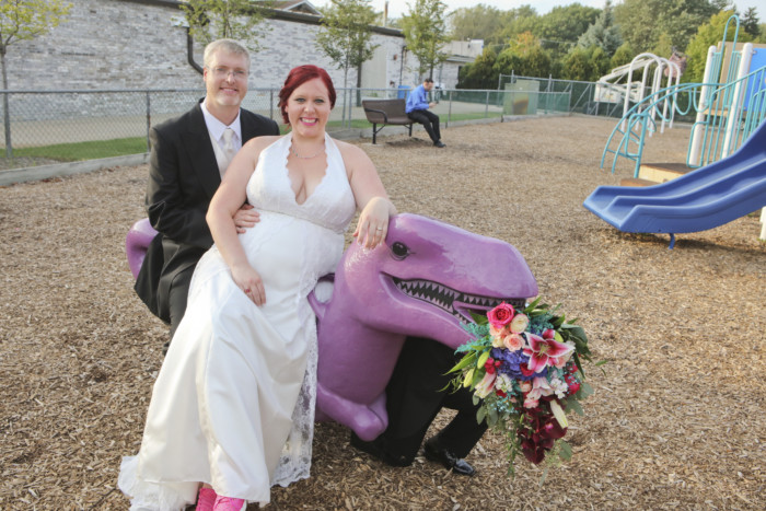 bride and groom sitting on a playground dinosaur eating the bridal bouquet