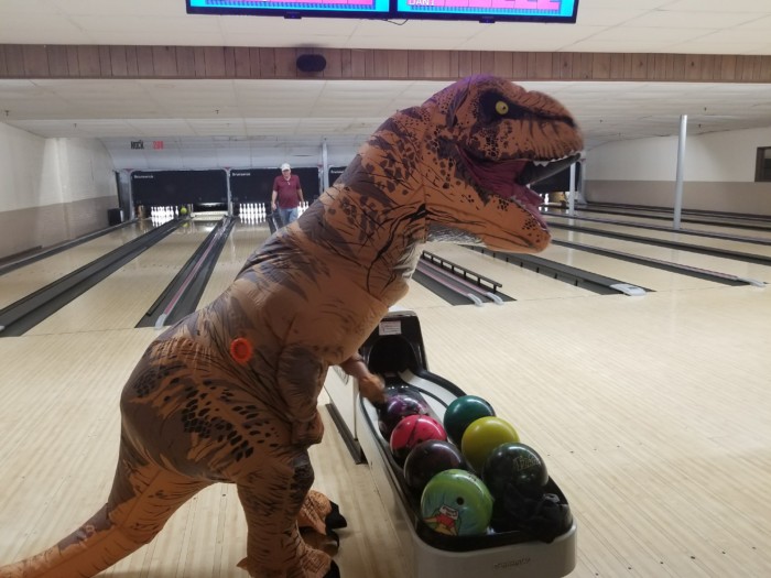 T-rex costume reaches for a ball at the bowling alley