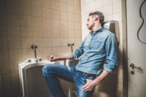 man falling asleep next to urinals