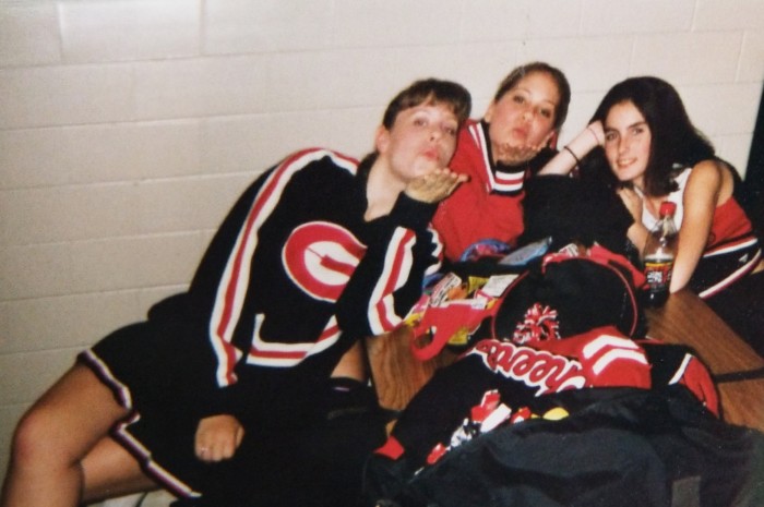 Three girls blowing kisses in 90s high school cheerleading uniforms