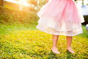 Unrecognizable little girl in pink princess skirt running barefoot in green sunny summer garden