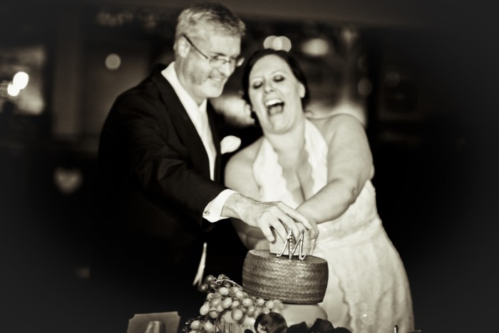 hilarious professional wedding photos laughing while cutting the cheese wedding cake made of cheese wheels