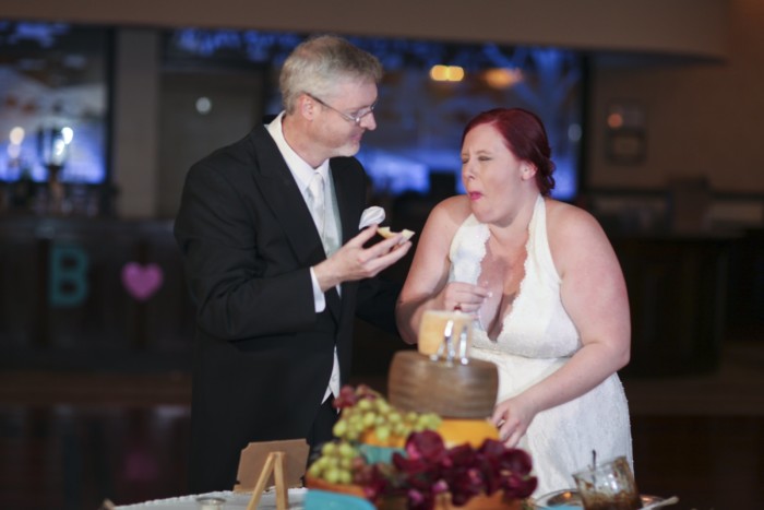 hilarious professional wedding photos laughing while cutting the cheese wedding cake made of cheese wheels