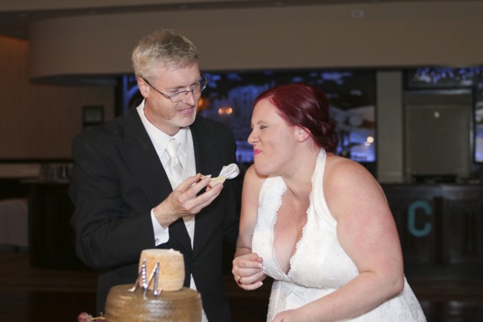 hilarious professional wedding photos laughing while cutting the cheese wedding cake made of cheese wheels