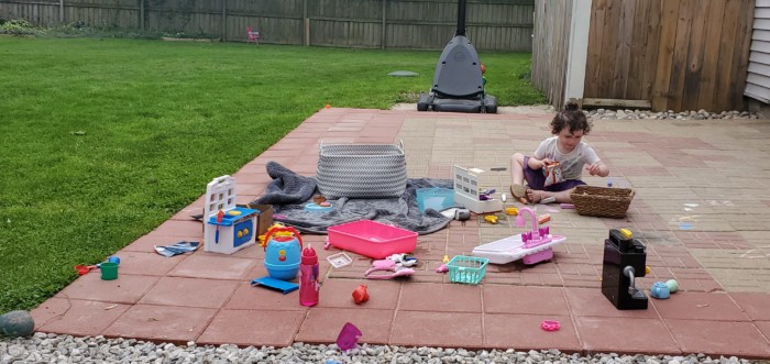 Toddler niece surrounded by toys in a backyard patio